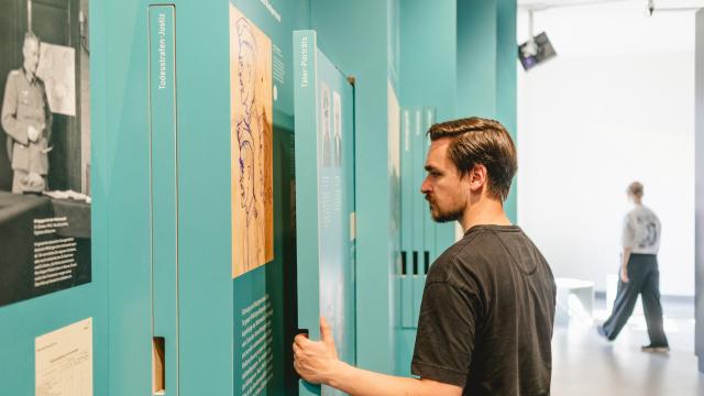 Ein Besucher steht in der Ausstellung und betrachtet eine Texttafel