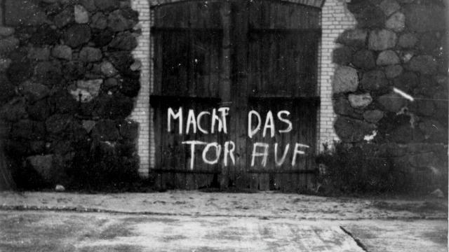 Das Bild zeigt ein Scheuentor, auf dem mit weißer Farbe geschrieben steht "Macht das Tor auf"