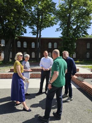 Gruppe von fünf Besuchenden stehen am neuen Gedenkort am Brückenkopf und sind in ein Gespräch vertieft.
