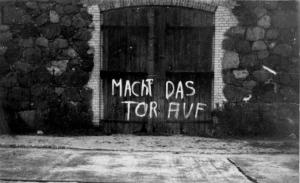 Das Bild zeigt ein Scheuentor, auf dem mit weißer Farbe geschrieben steht "Macht das Tor auf"